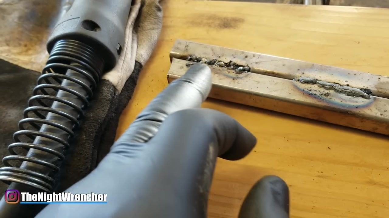A gloved hand demonstrates the correct stick-out distance with a pinching gesture above the welded metal bars.