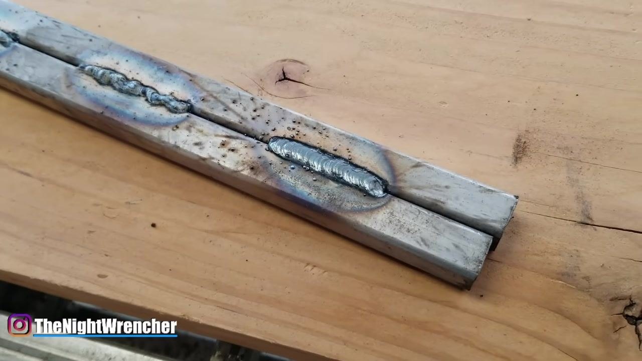 A gloved hand gestures toward welded metal bars on a wooden workbench, emphasizing the presence of slag on the welds.