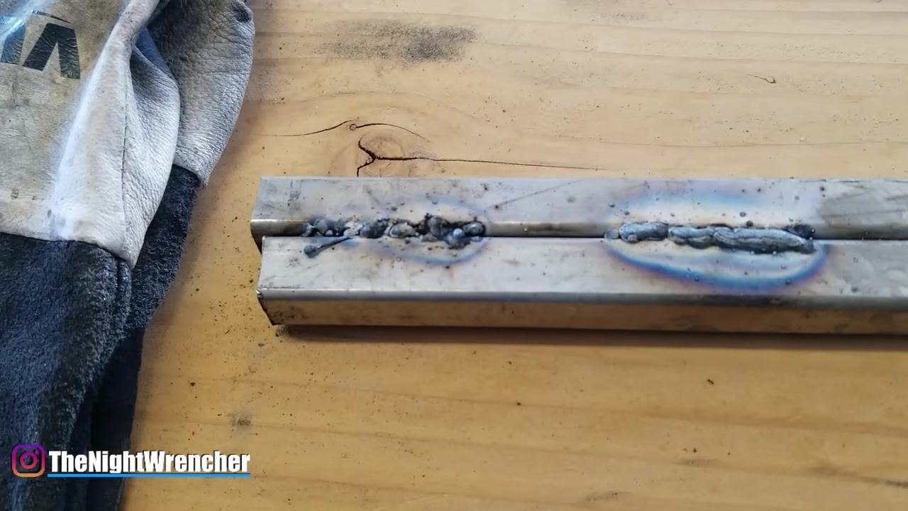 MIG gun pointing at the first weld on a metal sample, demonstrating the effect of holding the gun too far away.