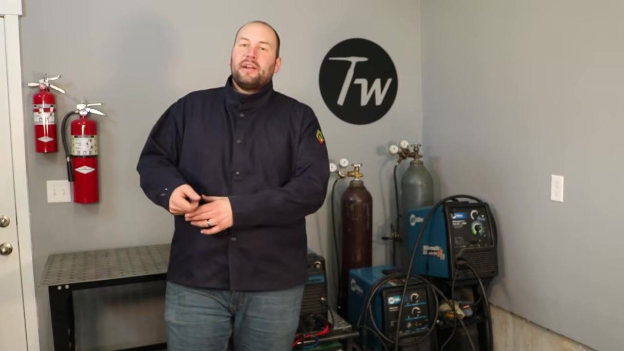 Instructor in a welding workshop, standing near fire extinguishers, gas cylinders, and welding machines, emphasizing the importance of mastering one welding variable at a time