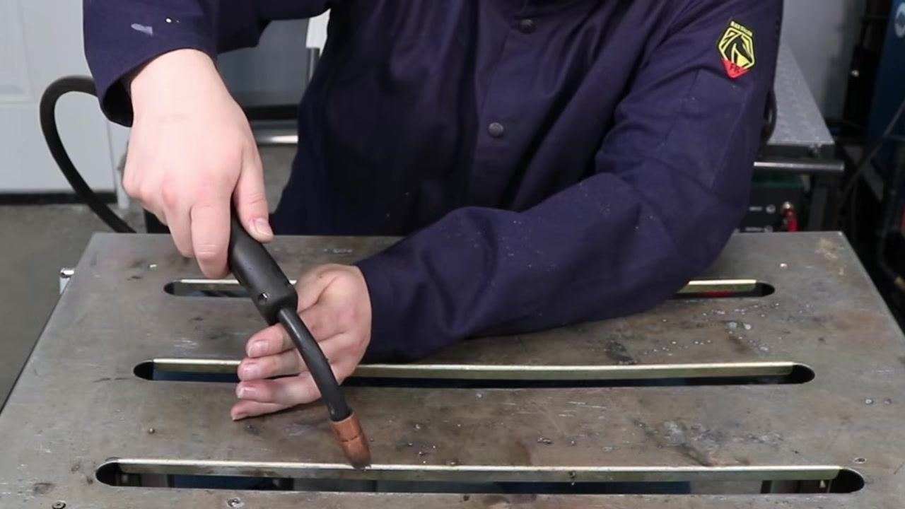 Welder demonstrating the MIG gun held too close to the workpiece, illustrating the risk of burning the wire back into the contact tip