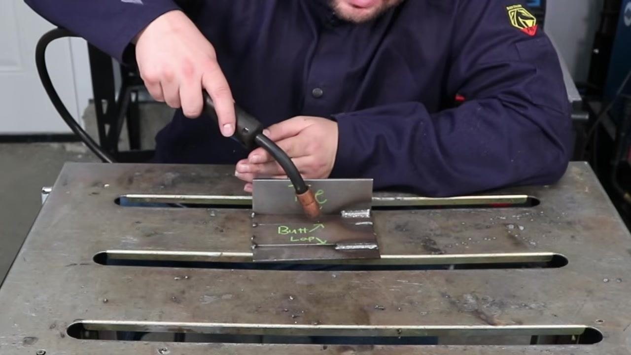 Welder performing a dry run along a T-joint, maintaining both the correct work angle of 45 degrees and a slight push travel angle, with the MIG gun positioned over the labeled plates