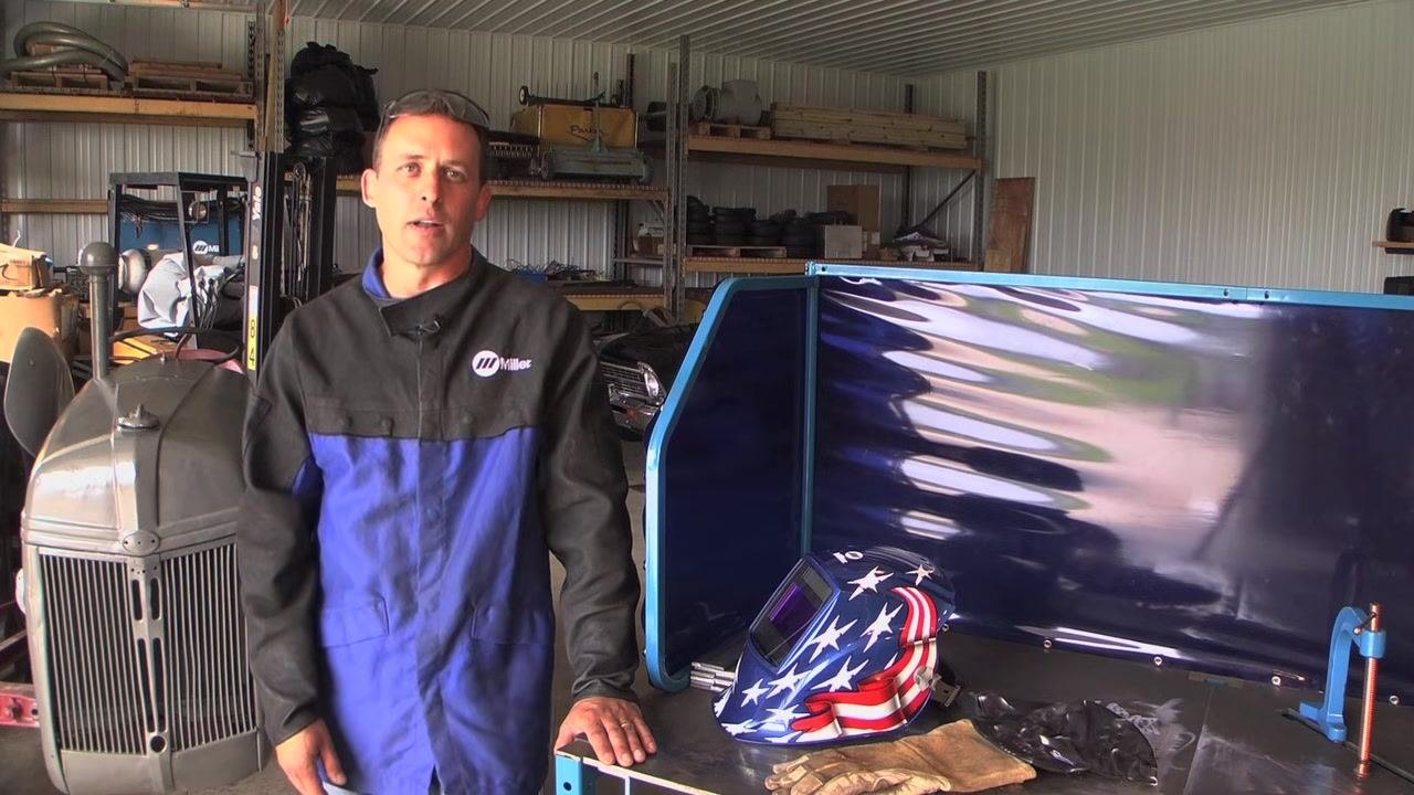 Instructor next to a welding table with a welding helmet and gloves, emphasizing the importance of practicing on scrap metal