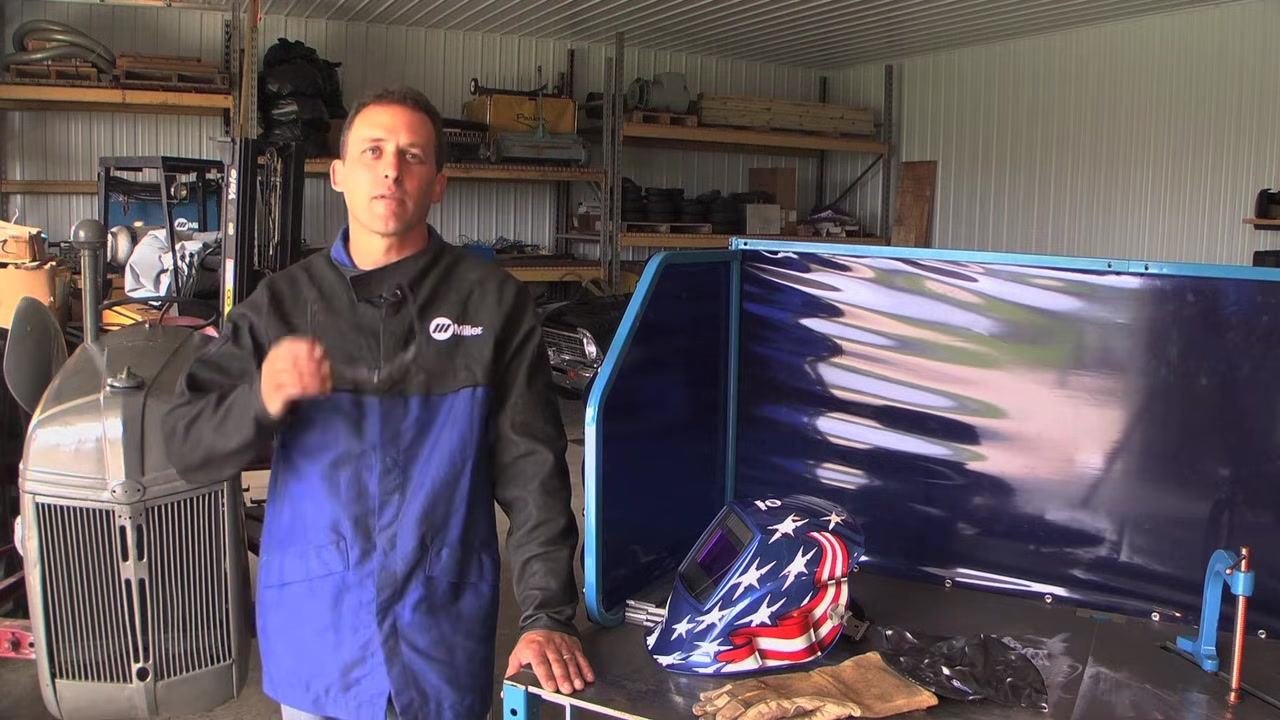 Instructor holding safety glasses, with a welding helmet and gloves on the table, emphasizing the importance of safety gear