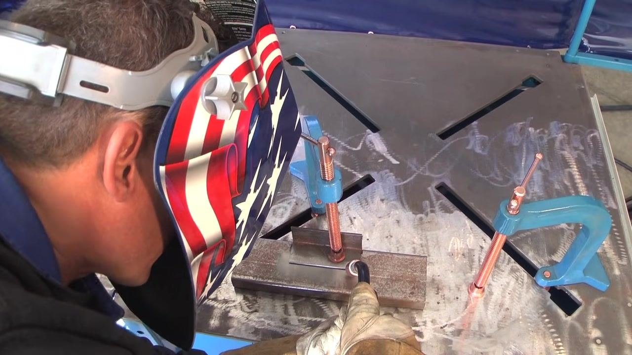Welder wearing a helmet, positioned to weld with the gun at the correct angle, workpiece clamped and ready