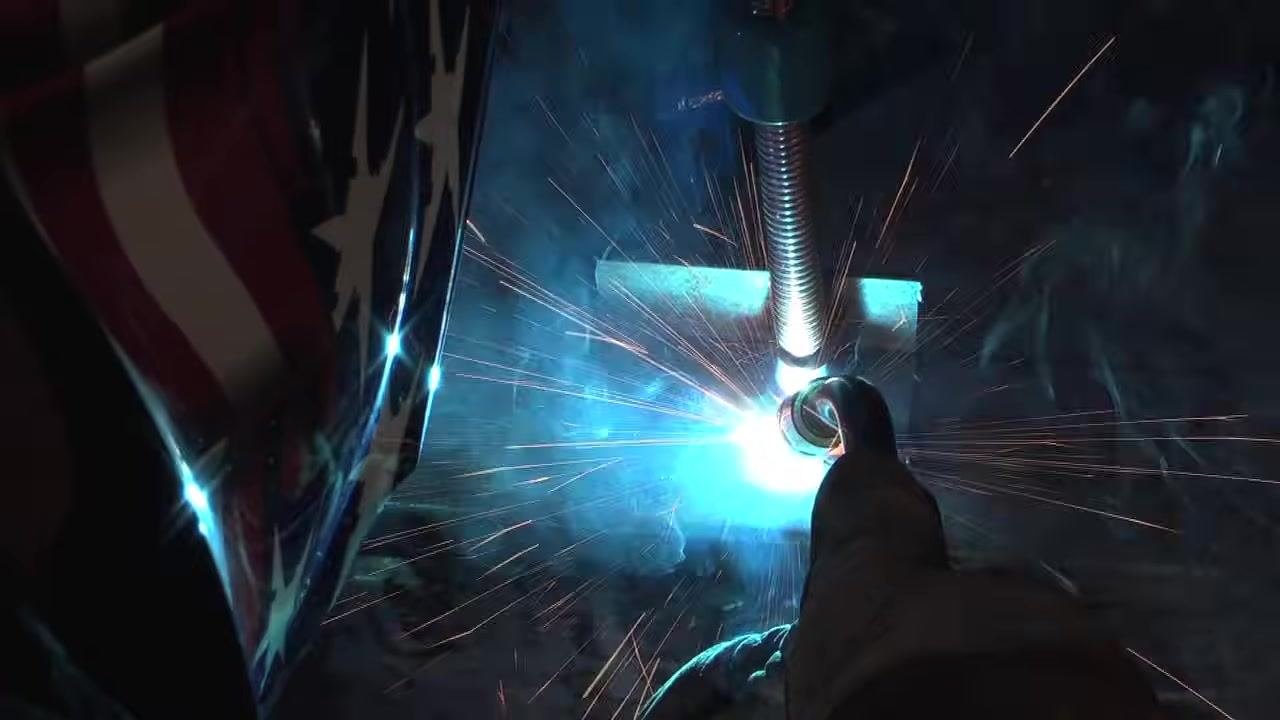 Welder with helmet and gloves making a straight weld on a lap joint, gun angled toward the bottom workpiece