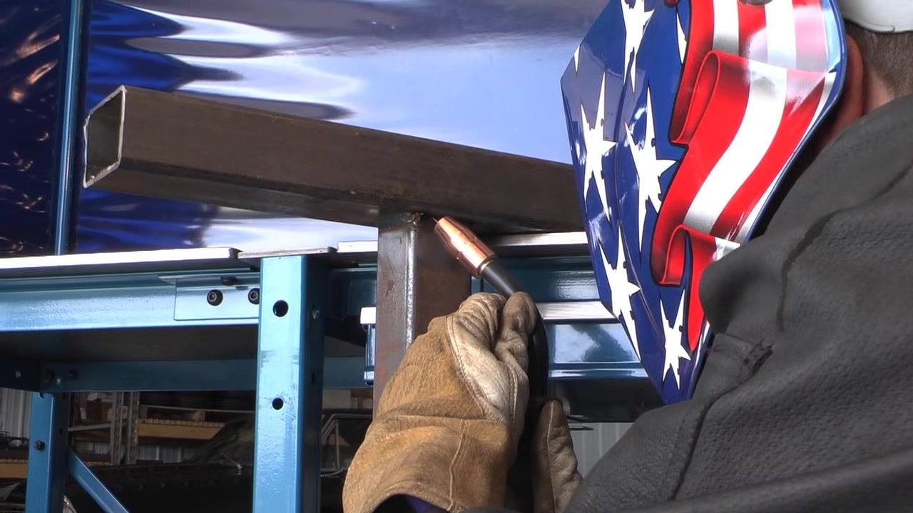 Close-up of a vertical weld bead on thick, rusted rectangular steel tubing, showing the result of a vertical up weld