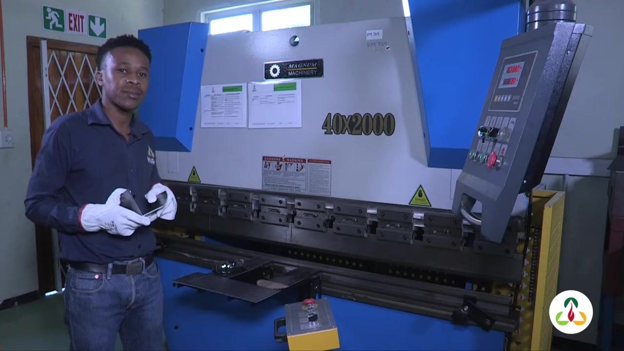 Operator holding a metal plate with marked lines, standing in front of the press brake