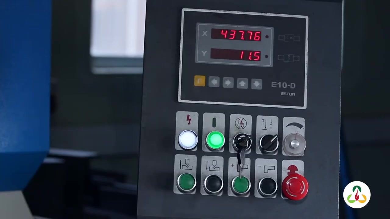 Close-up of gloved hands positioning the metal plate on the press brake bed. Emergency stop and control box visible.