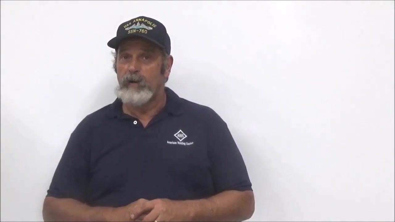 Instructor in navy shirt and cap, standing in front of a whiteboard, speaking and gesturing to the audience