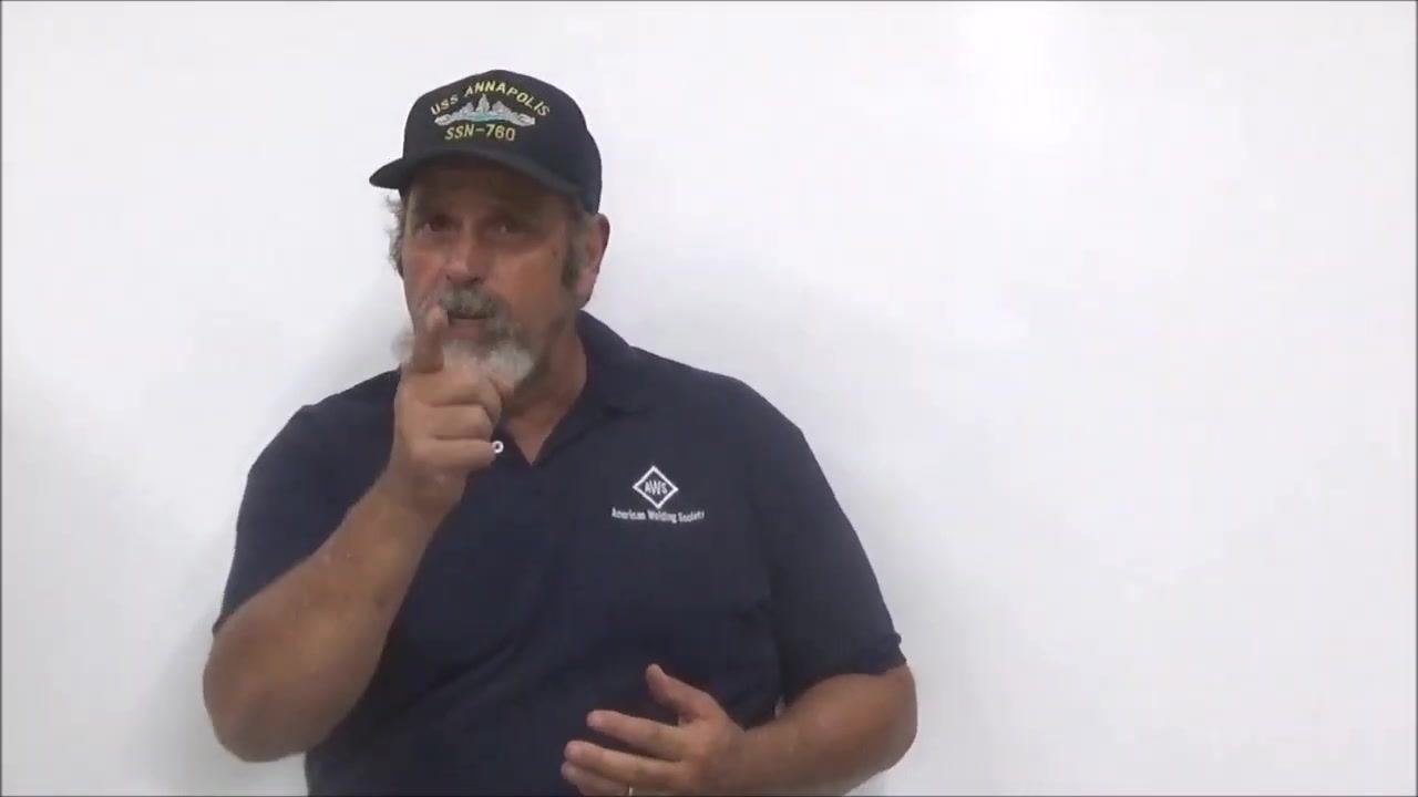 Instructor in front of a whiteboard, wearing a navy shirt and cap, gesturing and speaking to the audience
