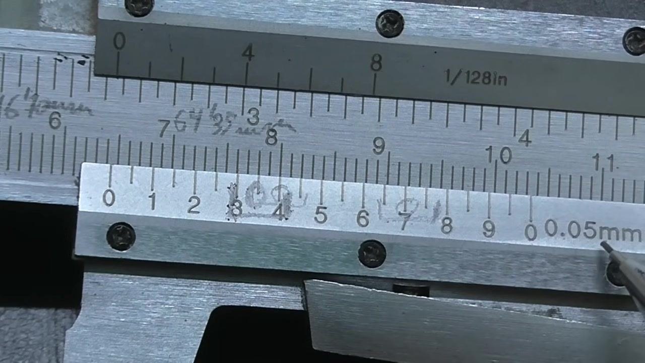A hand holding a pen points at the 7th line on the vernier scale, the middle of the three coinciding lines.