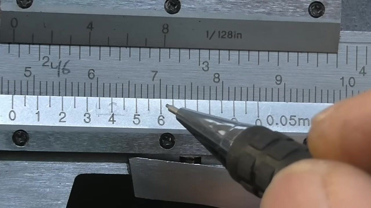 Vernier caliper with a pen pointing along the vernier scale while searching for the three best-coinciding lines.