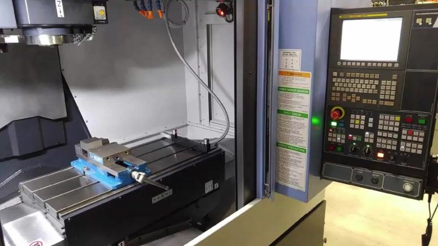 Doosan vertical mill with Fanuc I-Series control, vise mounted on the table, control panel visible, safety and operating instructions posted