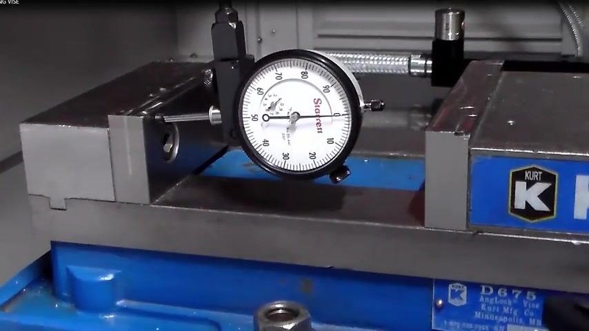 Close-up of a Starrett dial indicator contacting the solid jaw of a Kurt vise, showing a reading, vise mounted on a blue base