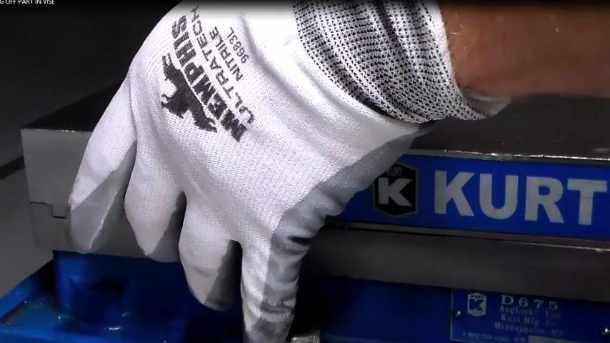 Gloved hand placing a parallel against the solid jaw of a Kurt vise, vise open and ready for part loading