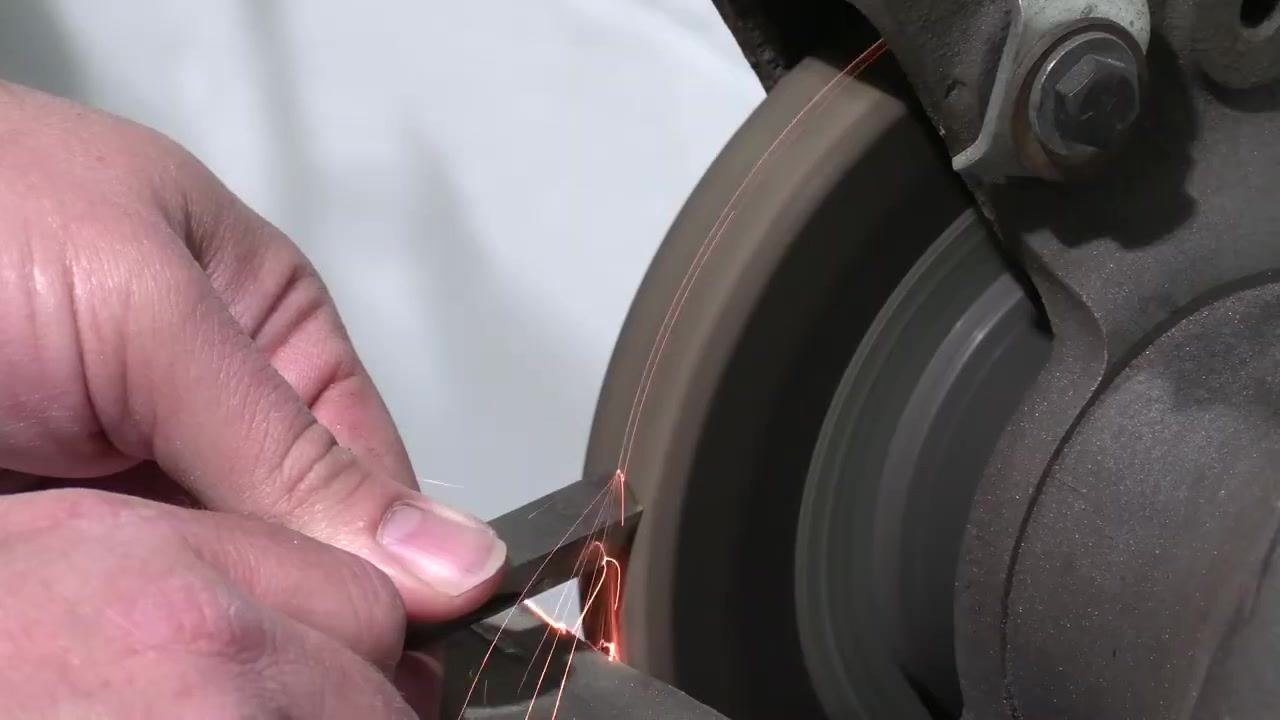 Hands hold the tool bit against the grinding wheel as sparks fly during shaping.
