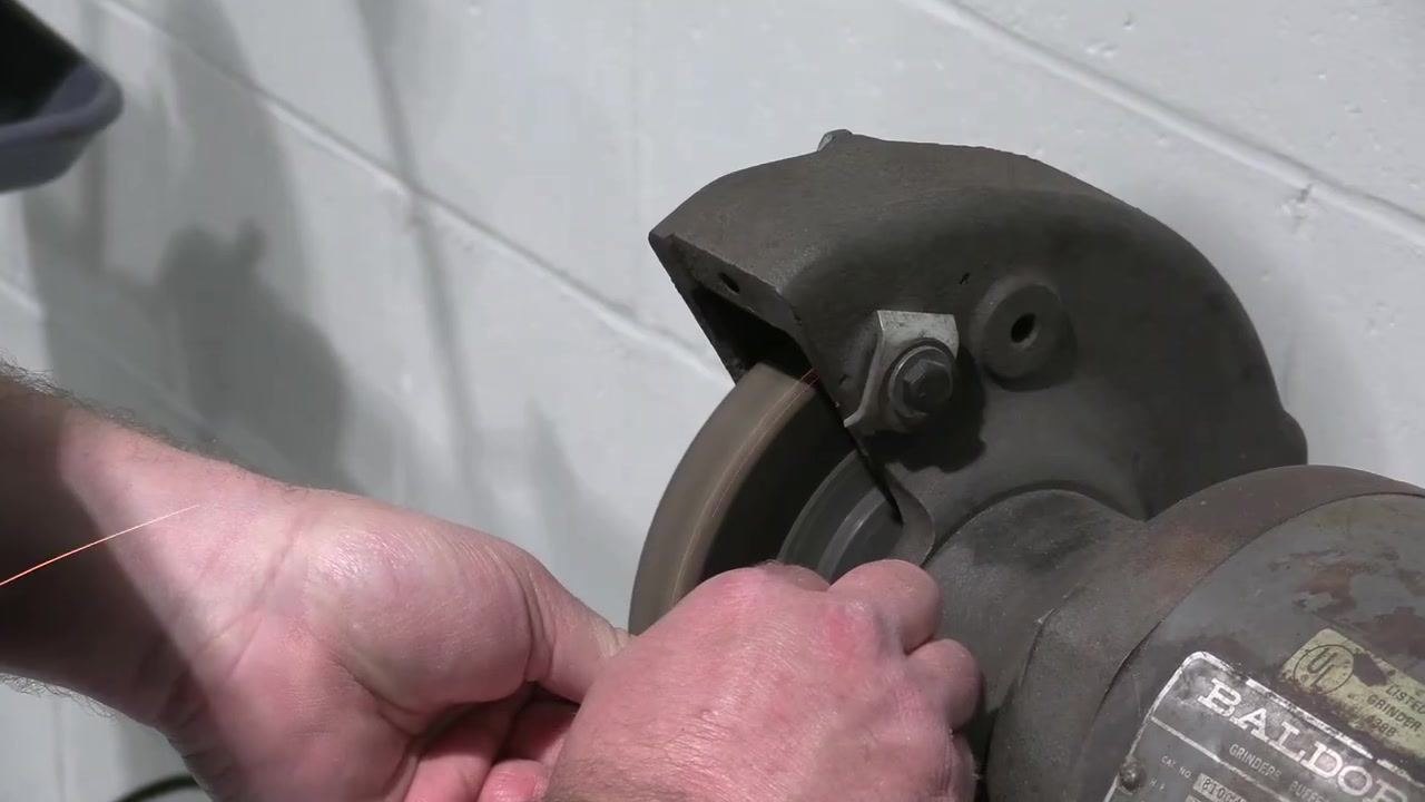 The tool bit is held against the spinning grinding wheel for a final shaping pass.