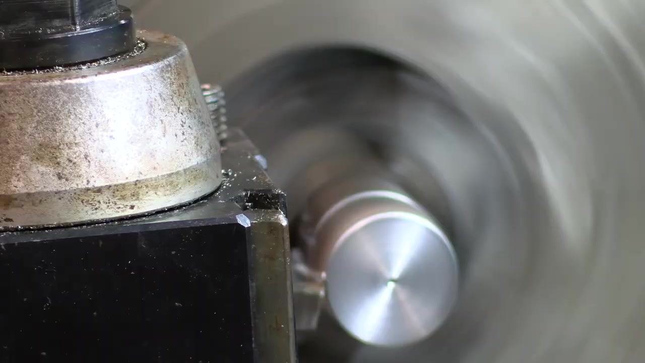 A close-up shows the lathe cutting tool engaging the spinning cylindrical workpiece, with visible chips and debris around the tool post.