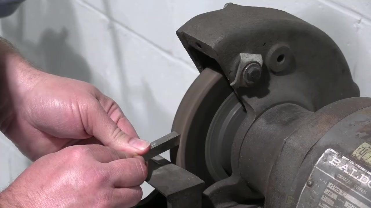 Hands hold the tool bit against the grinding wheel as sparks fly during grinding.