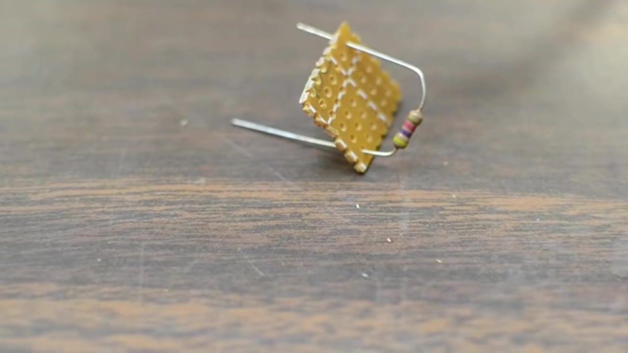 A soldering iron tip is held above a small prototyping board with a poorly formed solder joint, demonstrating incorrect soldering technique.