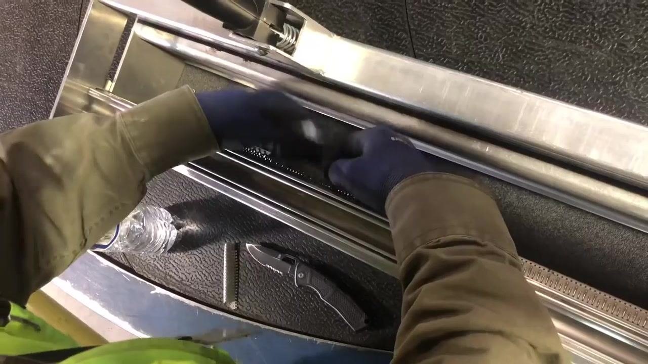 A worker's gloved hand engages the handle on the lacing machine, securing the belt in place.