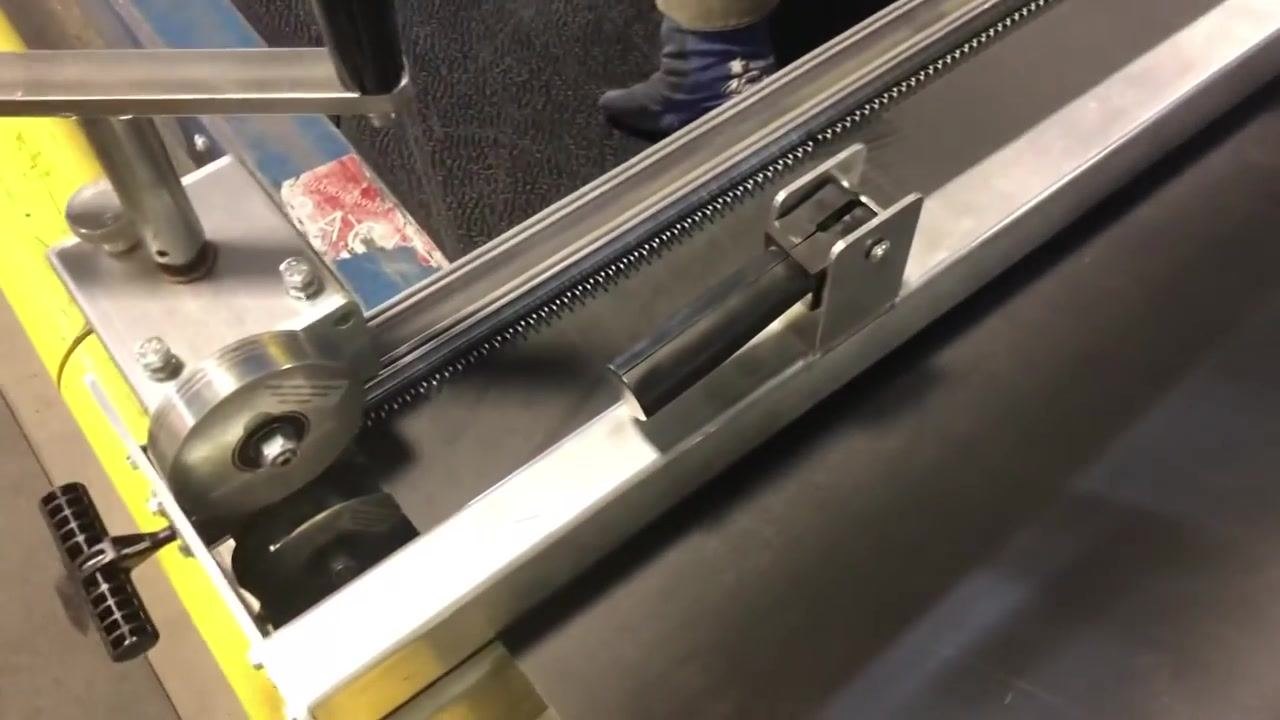 The lacing machine rollers are being closed so they just touch the belt and hooks, with the worker kneeling beside the machine.