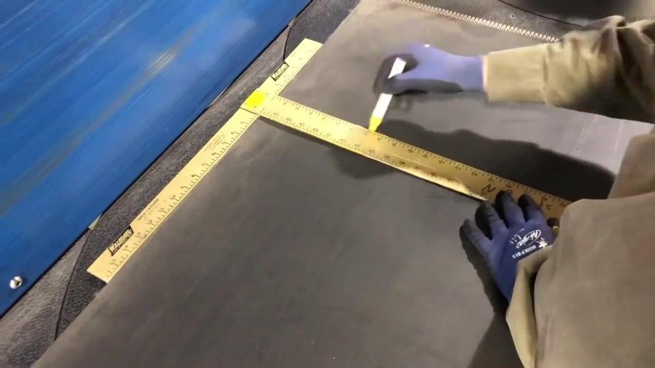 A gloved hand positions the top piece of the belt cutter over the conveyor belt, preparing for the cut.