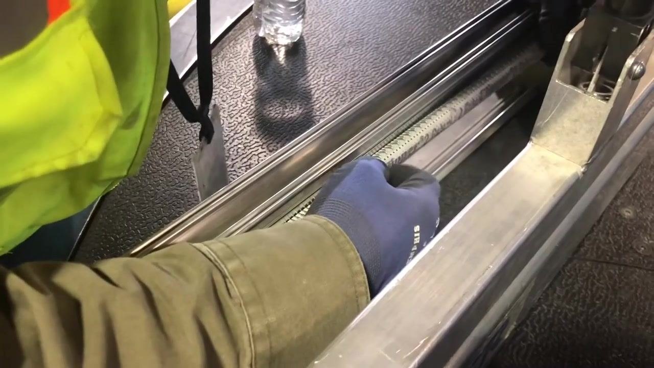 A worker pushes the correctly oriented hook into the lacing machine, preparing for the next step.