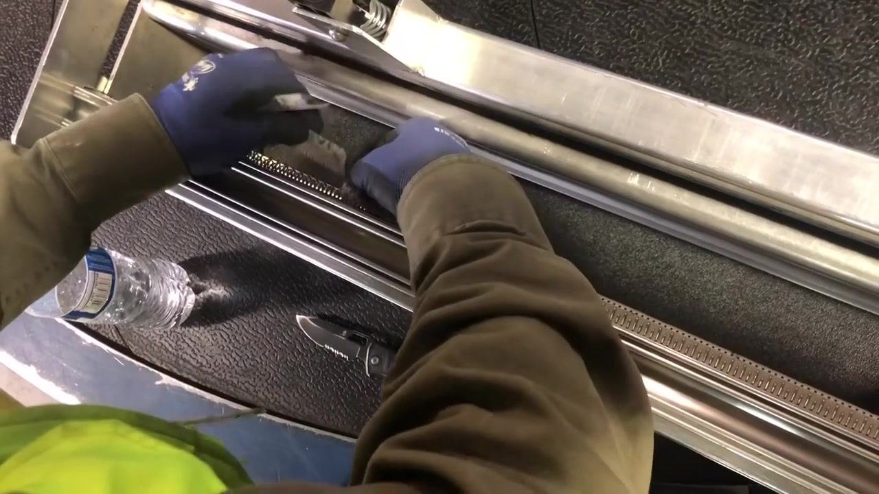 A worker in gloves squishes and removes paper from the lacing area of the belt lacing machine. The setup includes a water bottle and a utility knife nearby.