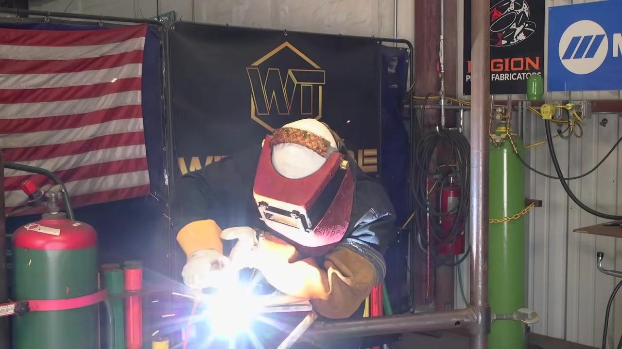 A welded plate shows a straight, uniform bead along the edge, with a gloved hand demonstrating the distance between the rod and the plate edge.
