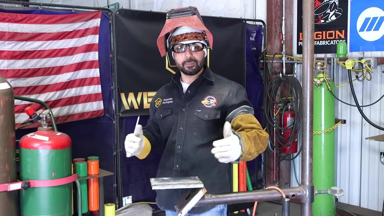 A welder in full safety gear holds a metal plate and welding rod, with gas cylinders and welding banners visible in the background.