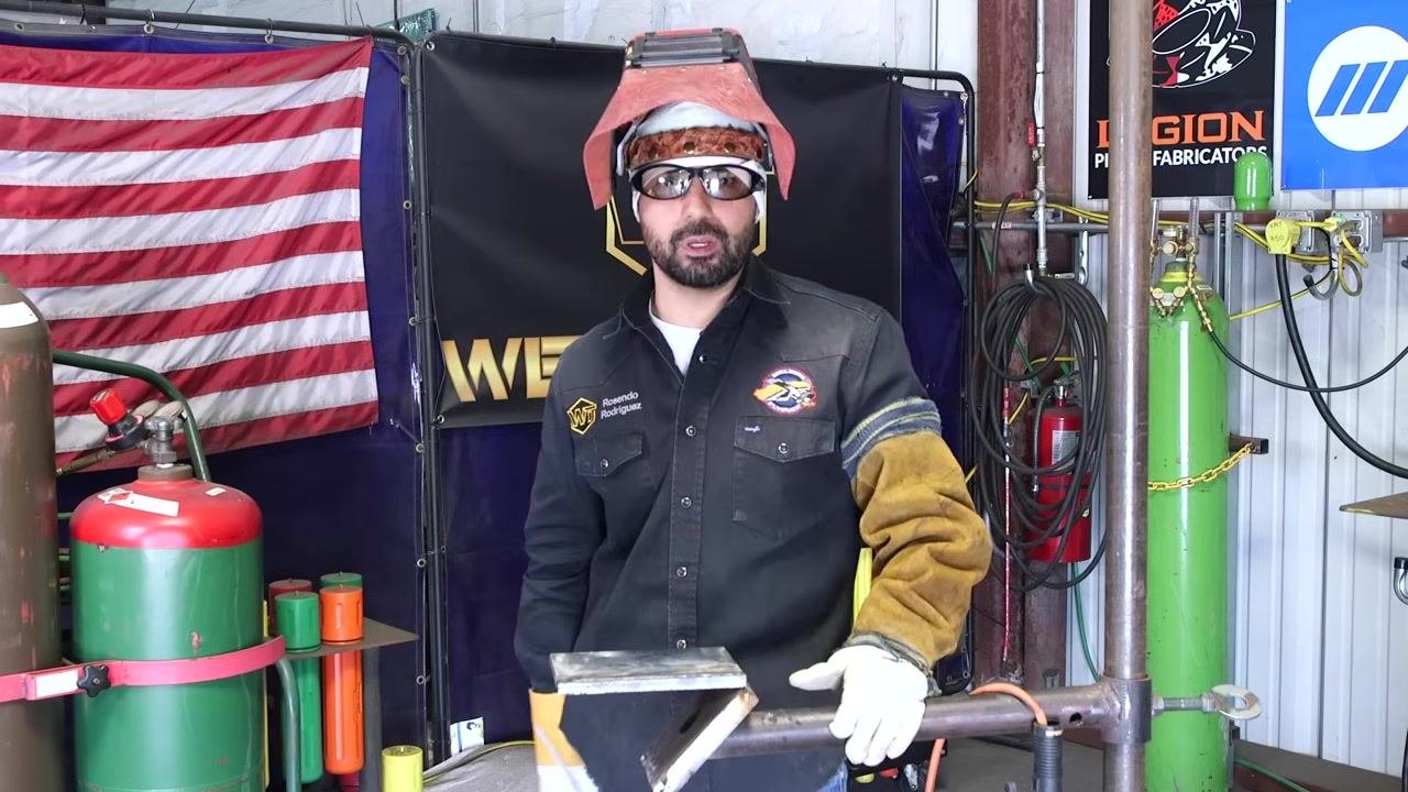 A welder demonstrates proper posture, holding the welding rod and plate while explaining the importance of not locking the knees.
