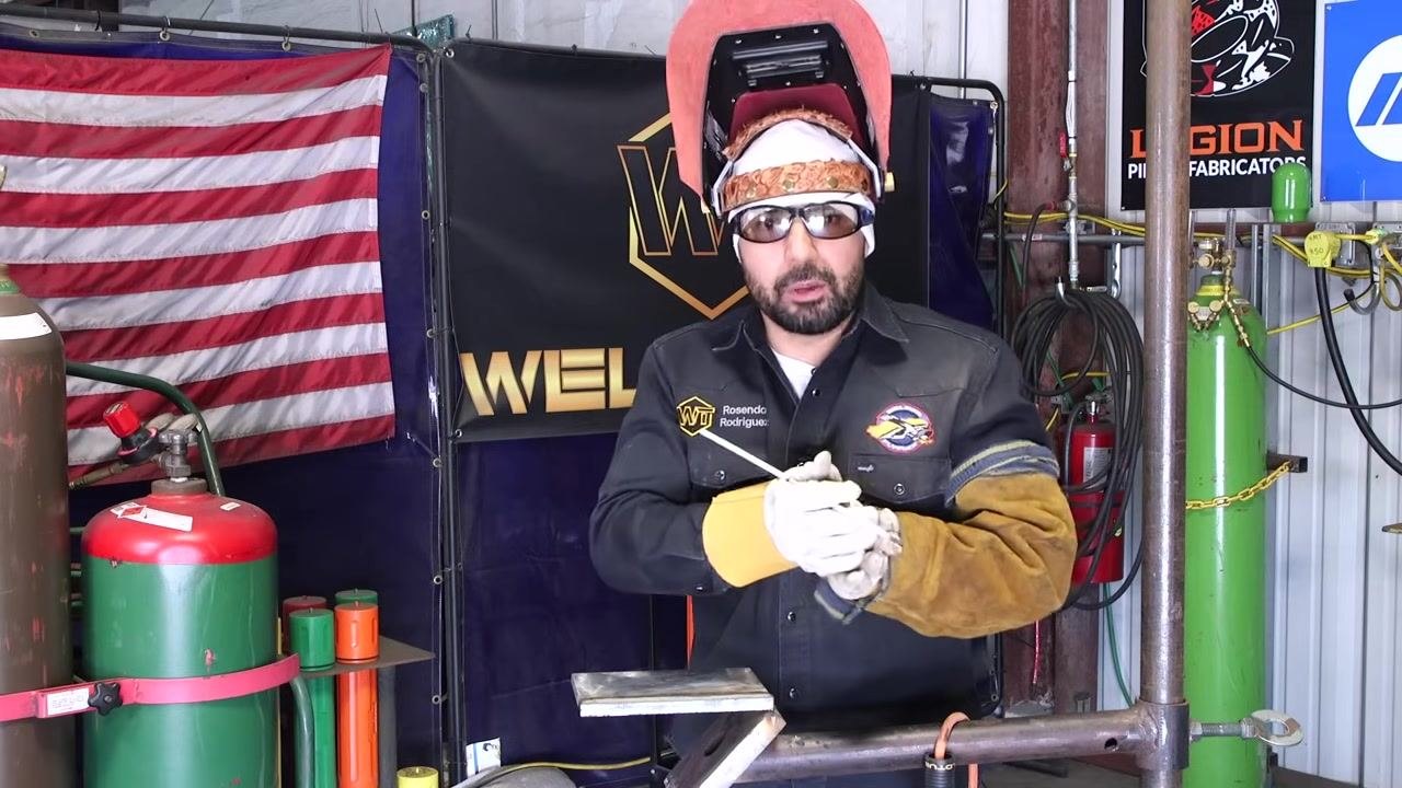 The rod is fed below the toe line during active welding, with visible sparks.