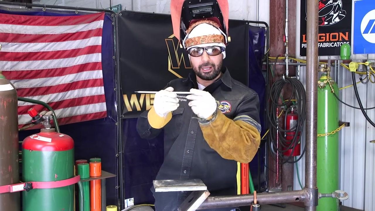 A welding rod is held horizontally to point out the flux coating and discuss its role in weld quality.