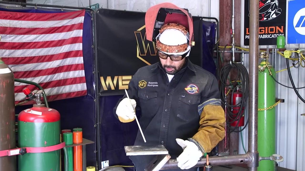A welder looks down at the workpiece, holding the rod above it, preparing to restart after identifying a weld defect.