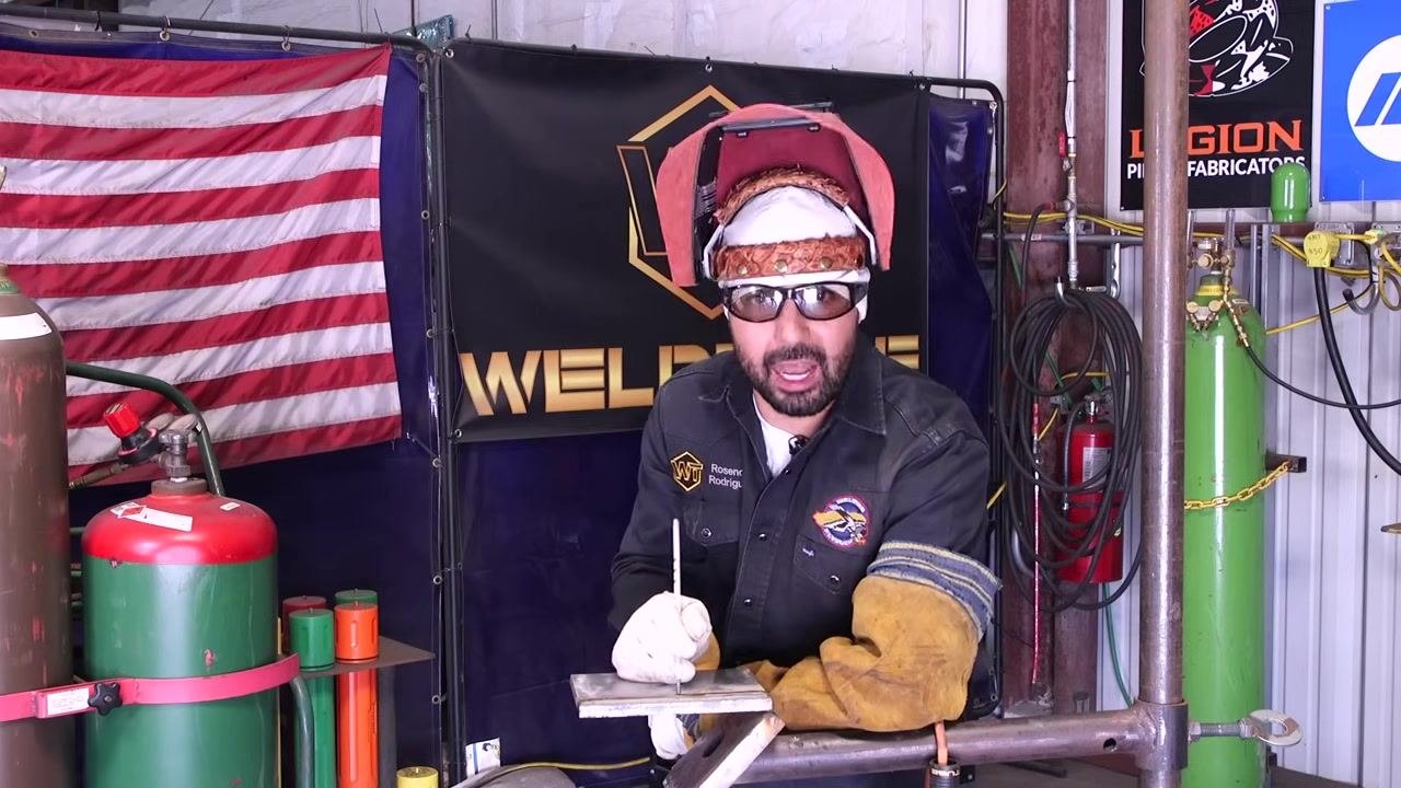 A welder leans in with the helmet down, ready to start welding.