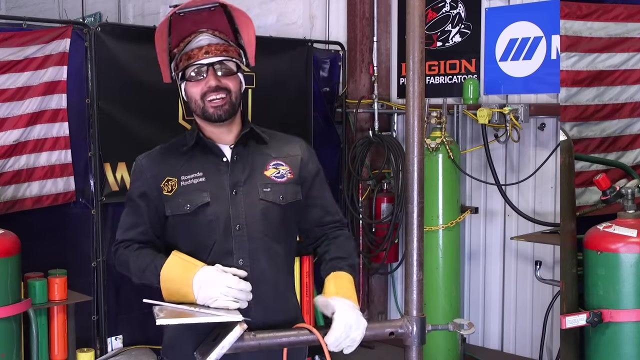 A welder wearing full PPE—jacket, gloves, safety glasses, and helmet—stands ready to begin welding.