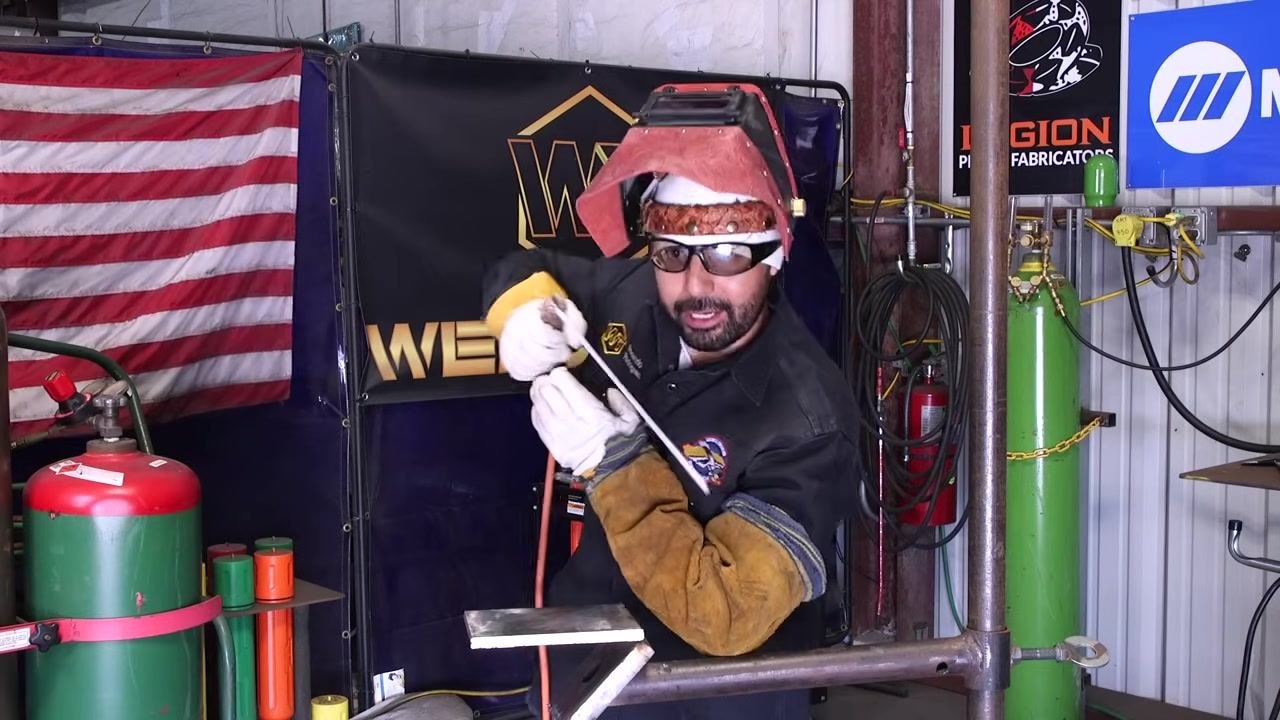 A welder moves the rod steadily while adjusting position to maintain a clear view of the weld.