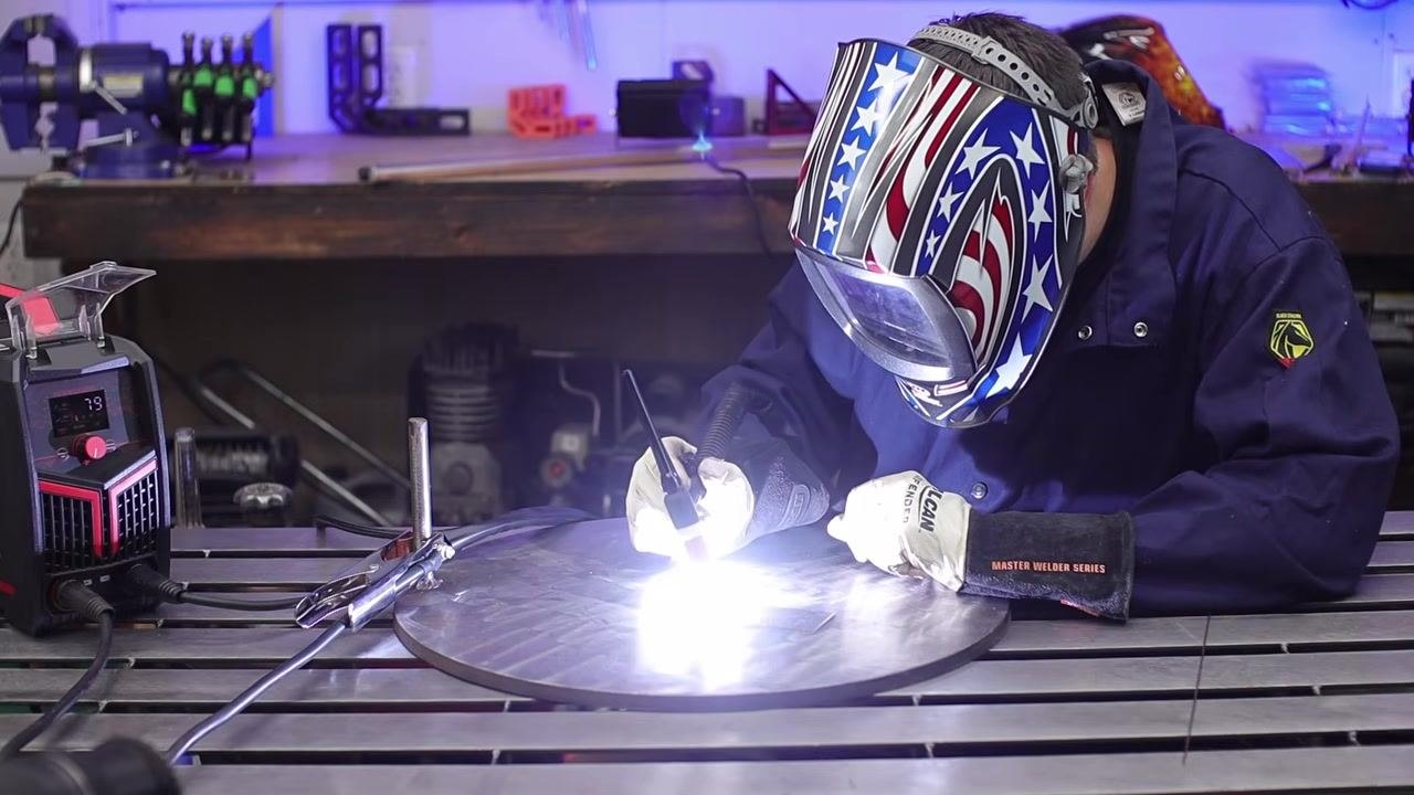 Welder adding filler rod to the weld pool with both hands engaged, arc visible, wearing full safety gear.
