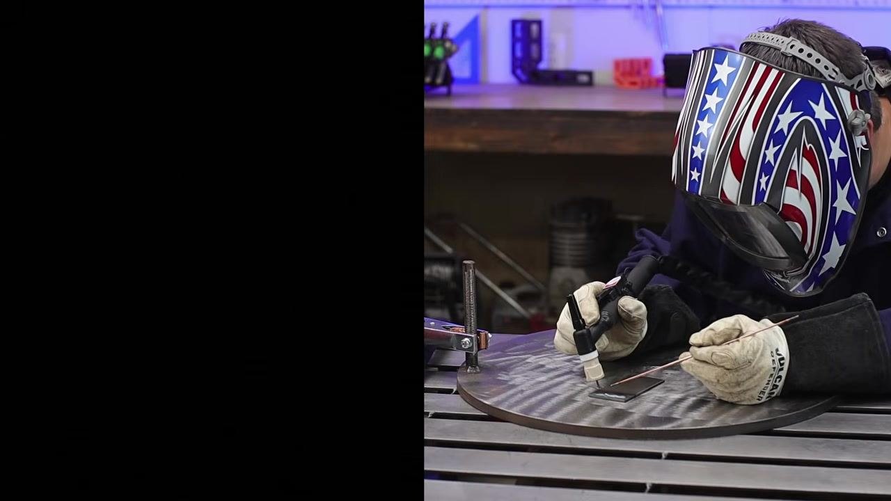 Person wearing a welding helmet and gloves positioning the torch and filler rod close to the workpiece, preparing to start the arc.