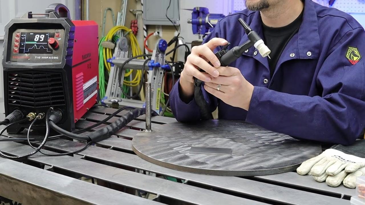 Close-up of a hand holding the TIG torch while explaining the solenoid and gas flow mechanism, with the welder and work area visible.