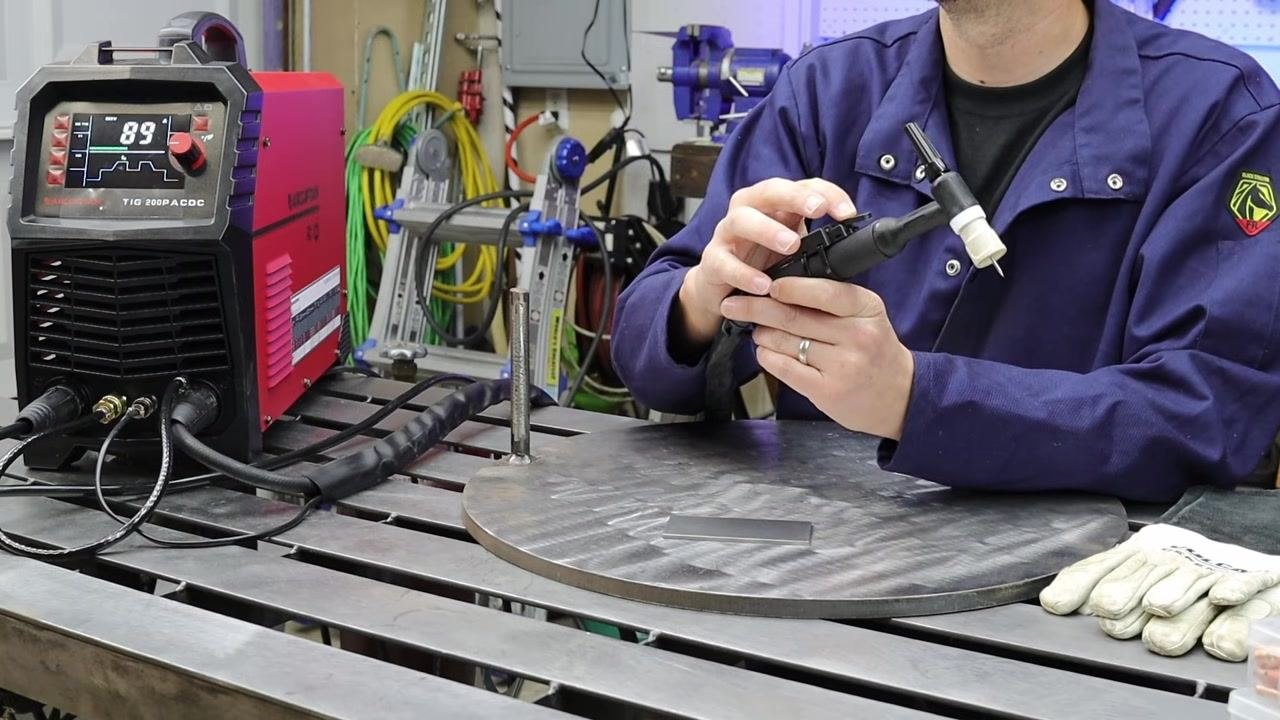 Person demonstrating the use of a foot pedal labeled "ARCCAPTAIN" as an alternative control method, holding the torch and pedal.