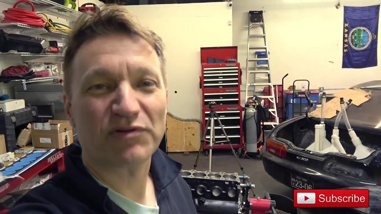 Close-up of a clean engine block deck showing the cylinder bores and machined surface, with a red tool chest and other garage equipment in the background.