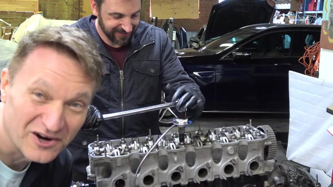 Two people at the engine: one preparing the torque wrench for the next round while the other looks on.