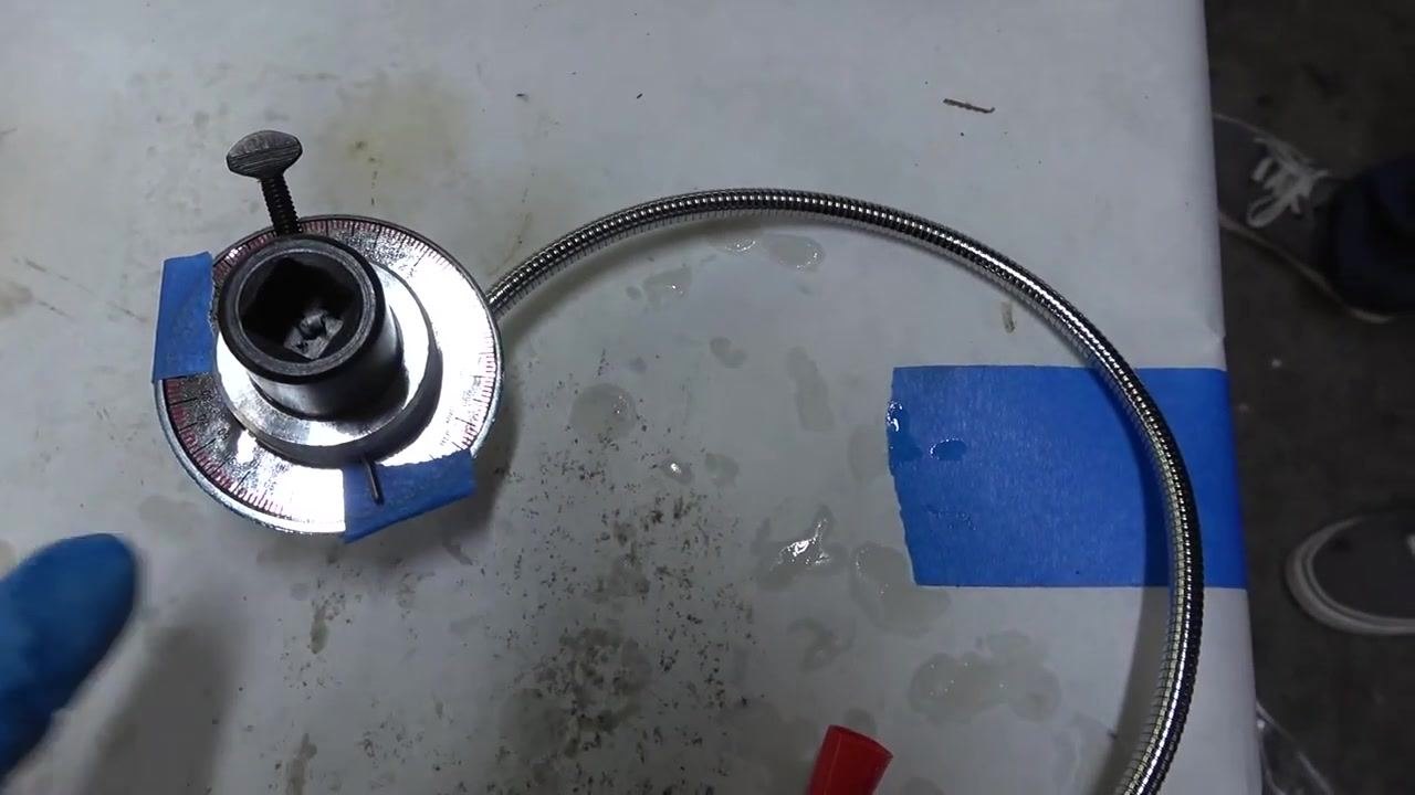 Torque angle gauge tool on a workbench, marked with blue painter's tape at the zero and 90-degree positions, showing the flexible arm and degree markings.