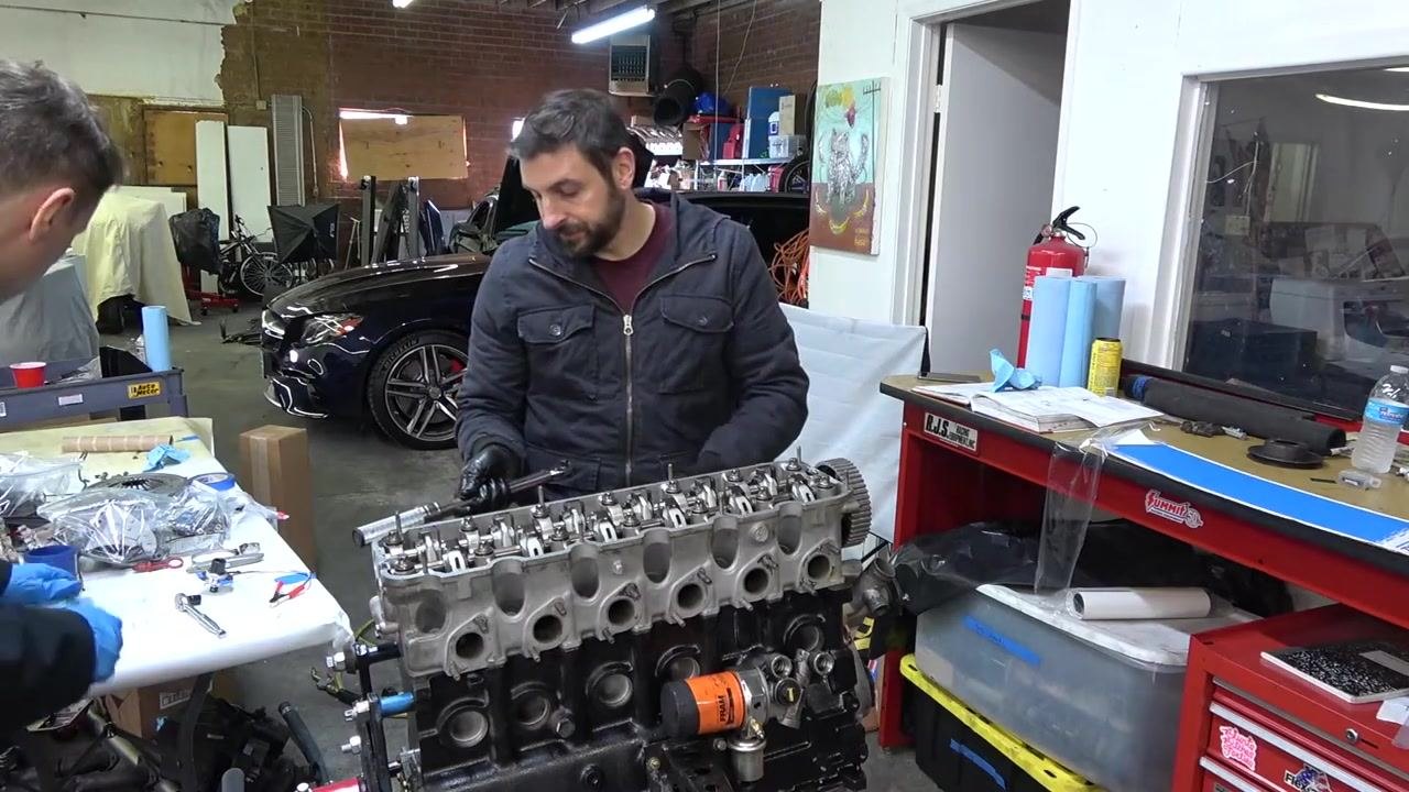Person holding a torque wrench, preparing to torque the head bolts on the installed cylinder head, with the engine, tools, and workspace visible.