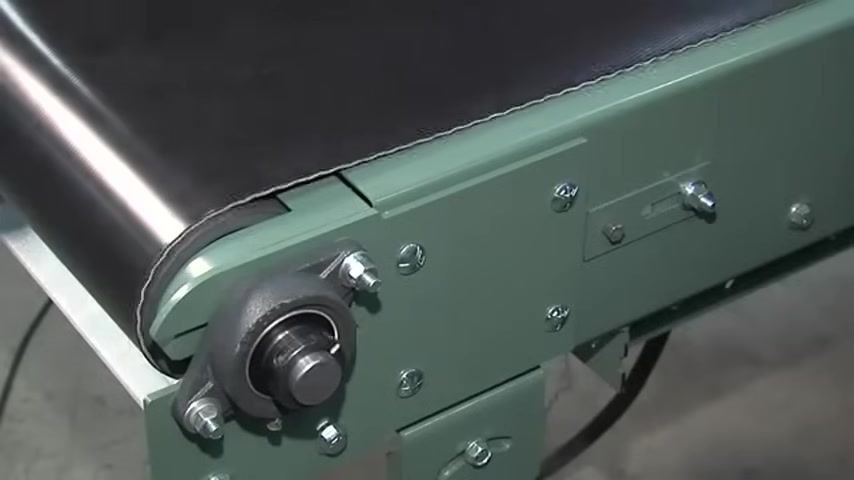 Belt drifting toward one side at the conveyor end, with a wrench held near the adjustment screw