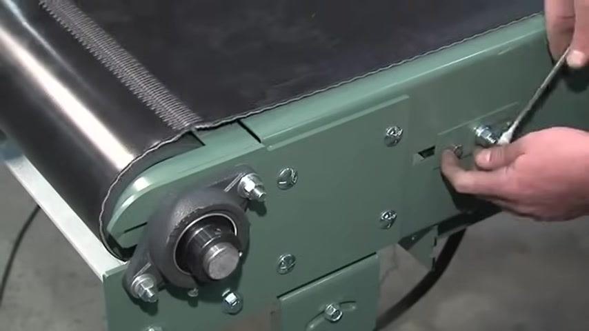 Adjustment screw and nut on the conveyor frame near the drive end, with a safety guard visible