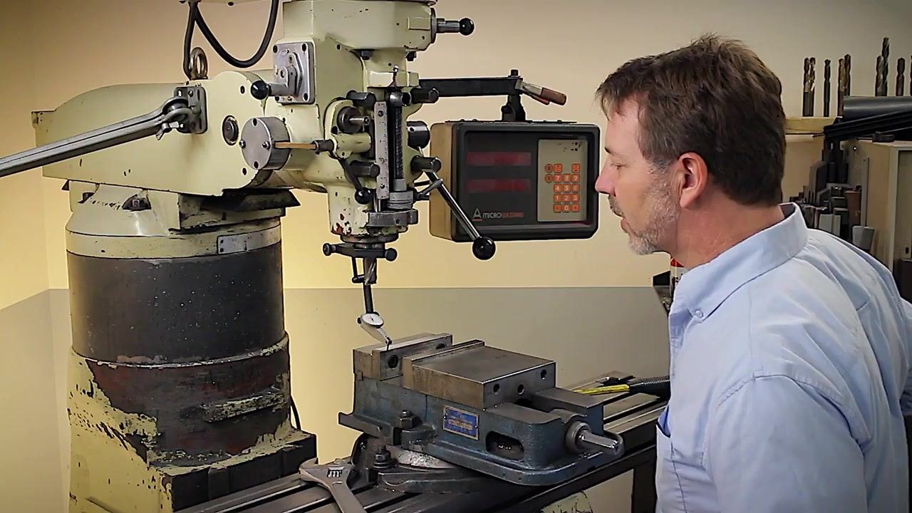The machinist checks the indicator and confirms the vise is trammed, with the digital readout and indicator setup clearly visible.